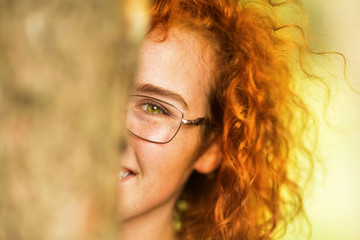 Beautiful young ginger woman hiding behind a tree