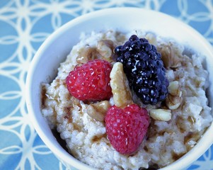 A toasty warm bowl of oatmeal with raspberries, blackberries and walnuts, drizzled with maple syrup