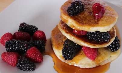 warm pancakes with raspberries and blackberries, drizzled with maple syrup