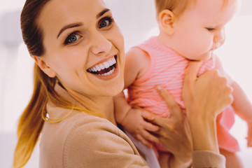 Holding a baby. Cheerful kind woman smiling and feeling excited while holding a baby girl after...
