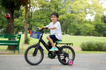 Fototapeta premium Asian cute boy ride a bicycle at park green nature background.Side view Image.