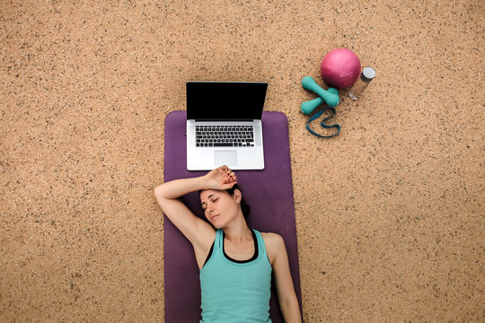 groggy and tired woman sleeping infront of a laptop on a yoga mat after doing an online fitness workout from bird view