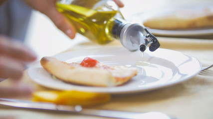 Female hands pours oil in plate to eat pizza in restaurant
