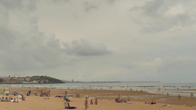 4 k Time-Laps frame posterise fasted video with view of Cnatabrian Sea city beach with speedy moving clouds, orange-brown sand, moving and laying people at the summer cloudy warm day