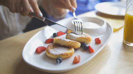 Female hands cuts a tasty cottage cheese pancakes with a knife and fork in restaurant