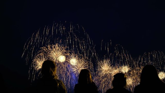 A crowd of people watching a big bright salute in the night sky, filmed on smartphones