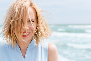 A middle-aged woman smiles with disheveled hair on vacation against the background of the sea.