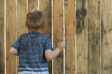 Curiosity of the child. A small boy looks into the crack of a wooden fence.