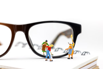Miniature people worker cleaning eyes glasses on book. Clear Vision concept.