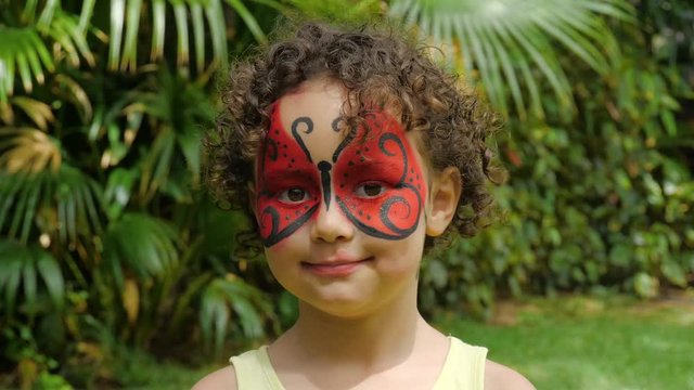 Young girl smiling into camera. With a ladybug butterfly face painting
