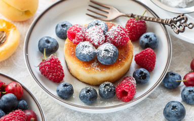 Cottage cheese pancakes, syrniki, curd fritters with fresh berries (raspberry, blueberry, apricot) and powdered sugar in a white plate.  Tasty and healthy  Breakfast