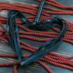 Scourge for BDSM in the form of a heart and a rope for binding on a dark background. Accesories for...