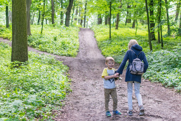 Two children walk along a forest path. The sister and the younger brother are going up the road in the forest.