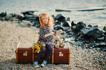 Sad child sitting on a suitcase and playing with his toy