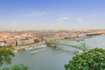 Fototapeta na wymiar Budapest skyline with red roofs of the buildings and the Liberty Bridge across the Danube and boats sailing on the river.