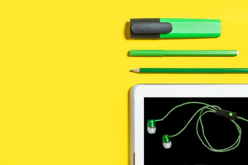 line of business or education accessories. green pencils, headphones, paper stickers, markers and tablet pc lying on a yellow surface. concept of the office chancery and gadgets. free copyspace