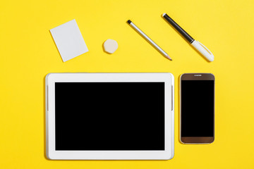 felt pen, pencil, rubber and paper stickers lying in front of smartphone and tablet pc at the yellow background. concept of office or educational stationary and gadgets. free copyspace. top view