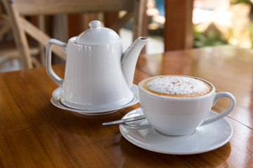 Cappuccino cup with tea pot on wooden table