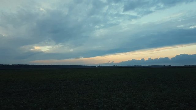 Field and forest in the amazing beautiful clorfull summer sunset. Beautiful thunder clouds over the field, shooting from a car that goes on the road along the ground. Evening, Dynamic scene, 4k video