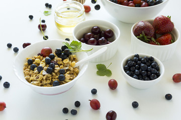 Bowl of homemade granola with strawberry, blueberry, cherry, gooseberry, black currant and honey on white wooden background. Flat lay. Copy space