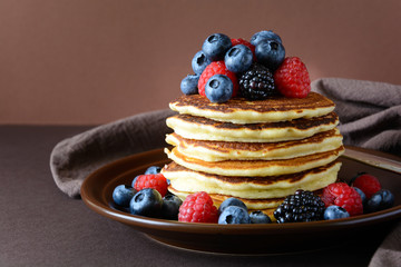 Stack of pancakes with fresh blueberry, raspberry and blackberry on brown plate