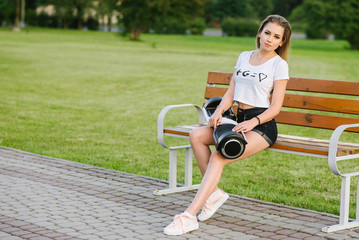Young happy woman sitting on bench and holding a hoverboard outdoors in the park