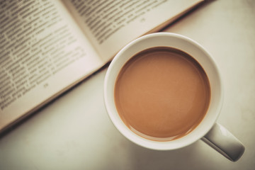 White cup with coffee next to an open book.