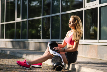 Young pretty woman in shorts and top sitthing with hoverboard on the street