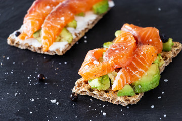 Two Crisp sandwiches with avocado and salmon. Slate background. Selective focus. Healthy breakfast concept.