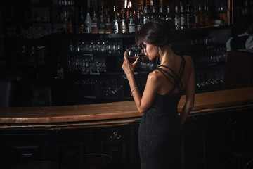 beautiful young brunette woman in black dress with glass of red wine in her hand