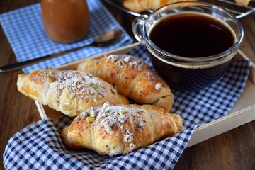 Fresh croissants sprinkled with nuts and a cup of black coffee