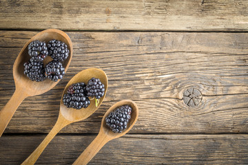 Freshly picked blackberries in the range of wooden spoons. Juicy and fresh blackberries on rustic table. Blackberry on wooden background.  Concept of healthy eating and nutrition for all family.