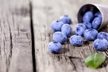 Juicy and fresh blueberries on rustic table, dropped out from silver cup. Blueberry on wooden background.  Concept of healthy eating and nutrition.