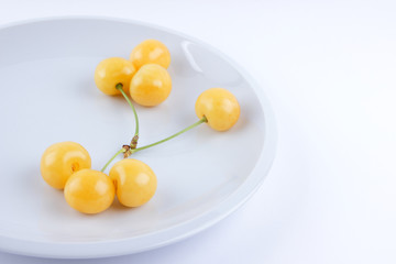Yellow cherries on white plate, fresh cherries on white background, yellow berries in minimalism style, vegetarian food, blank for designer, isolated