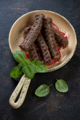 Serving pan with bbq cevapcici or balkan skinless beef sausages, vertical shot over dark brown stone background