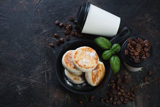 Curd pancakes or syrniki with takeaway coffee, high angle view on a dark brown stone background, copyspace, horizontal shot