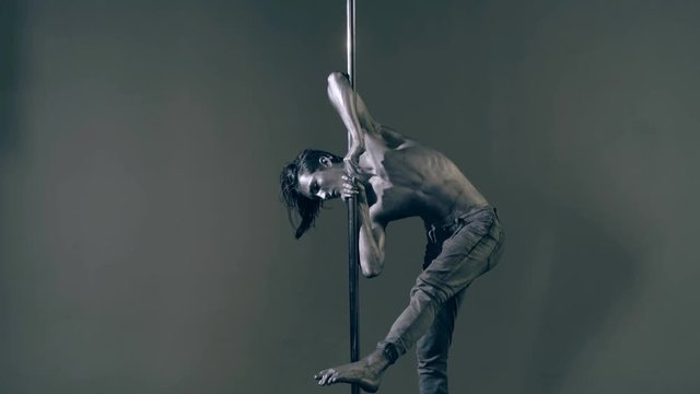 A guy with a gray body art makes tricks on the pylon. Pylon dance concept.