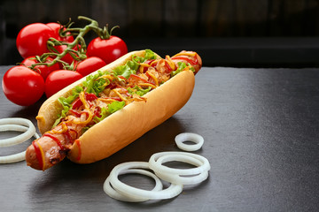 Hot dog with tomatoes and onion on dark slate background