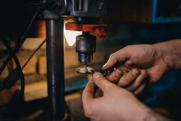 Man with his hands grinds small steel piece on shield under control.