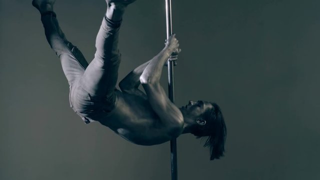 Pole dance concept. Fashion boy. Tricks on the pylon. The guy with a painted gray torso shows tricks on the pylon.