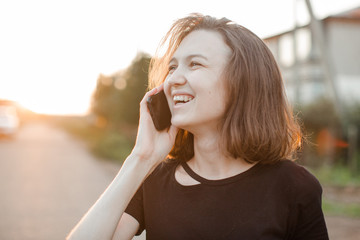 young girl with brown hair talking on the phone smiling and looking down at the sunset summer sun