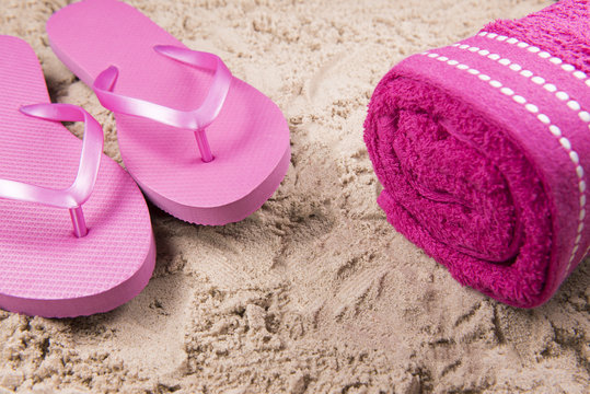 Beach background image of pink flip flops and a beach towel on a sandy beach 