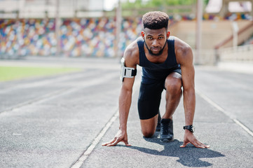 African american male athlete in sportswear racing alone down a running track at stadium.