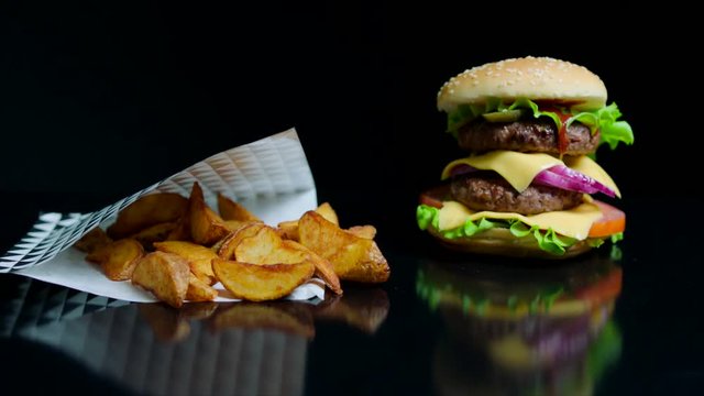 French fries and burger with double cheese and fresh greens on the black background