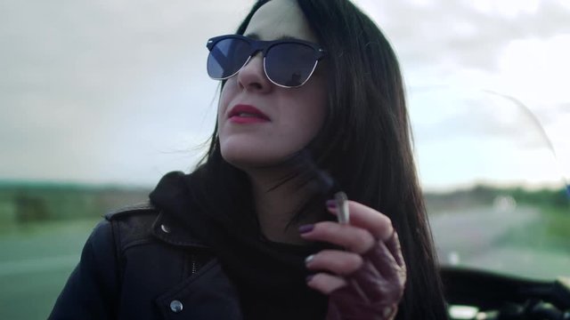 Woman biker in sunglasses and leather jacket is smoking