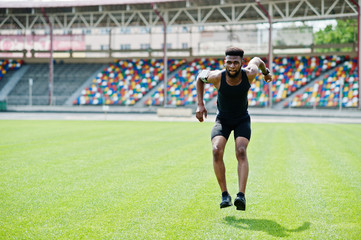 African american male athlete in sportswear doing jump exercise at stadium.
