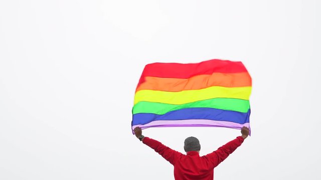 man raise rainbow flag LGBTI flag in hard wind with misty background
