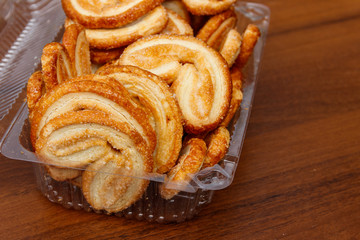 Palmier biscuits - french cookies made of puff pastry (also called palm leaves, elephant ears or french hearts) packed in plastic box on wooden table