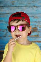 niño con gafas de sol y gorra chupando un caramelo con palo
