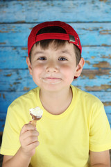 ni&ntilde;o con gorra roja tomando un helado en un fondo de madera azul